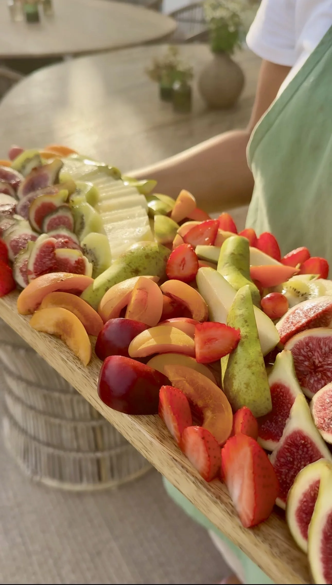 Campo catering staff in green apron presenting a colourful seasonal fruit platter on a wooden board at a Marbella villa event