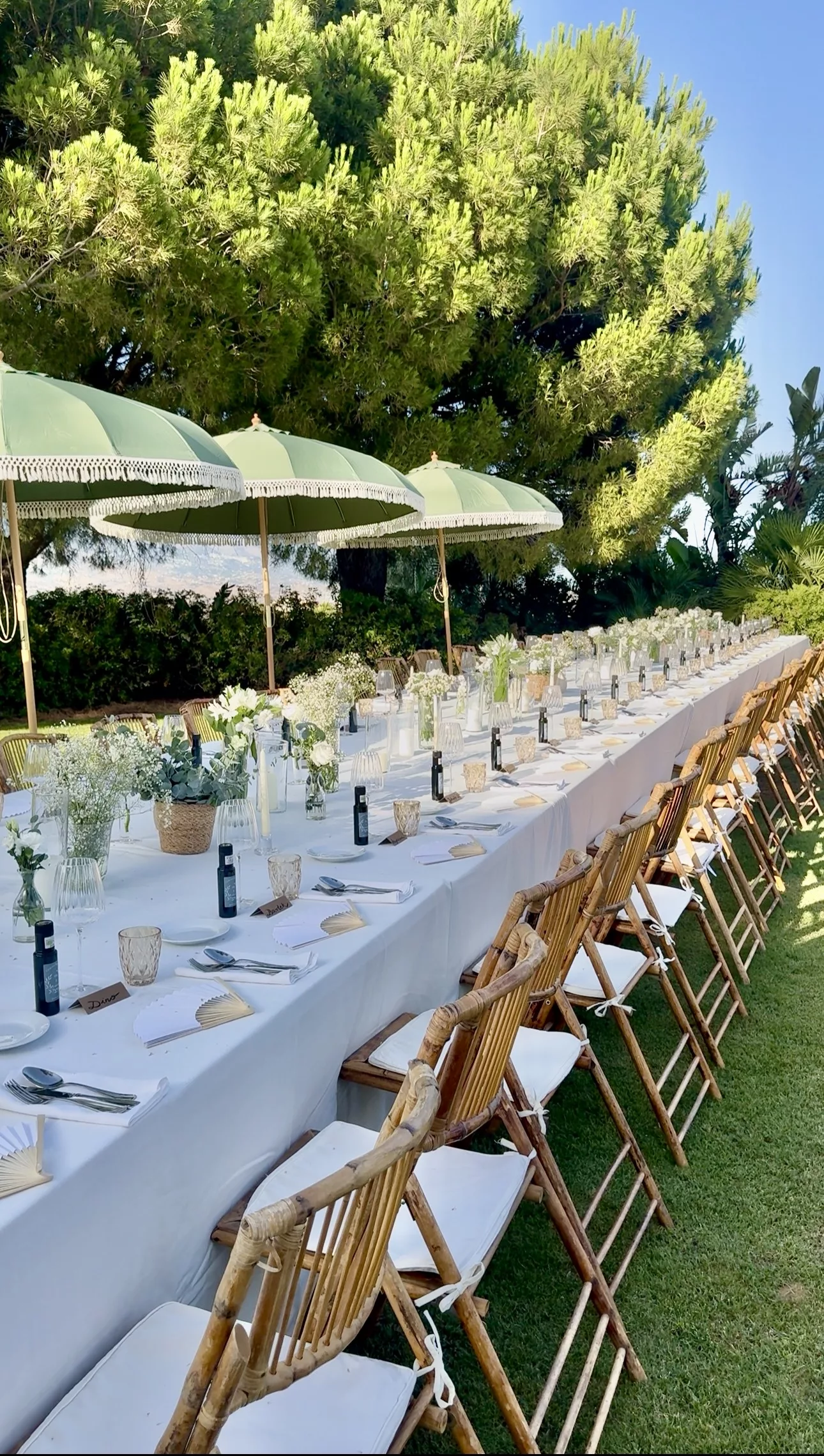 Long wedding table set outdoors with green parasols and bamboo chairs, private garden Marbella