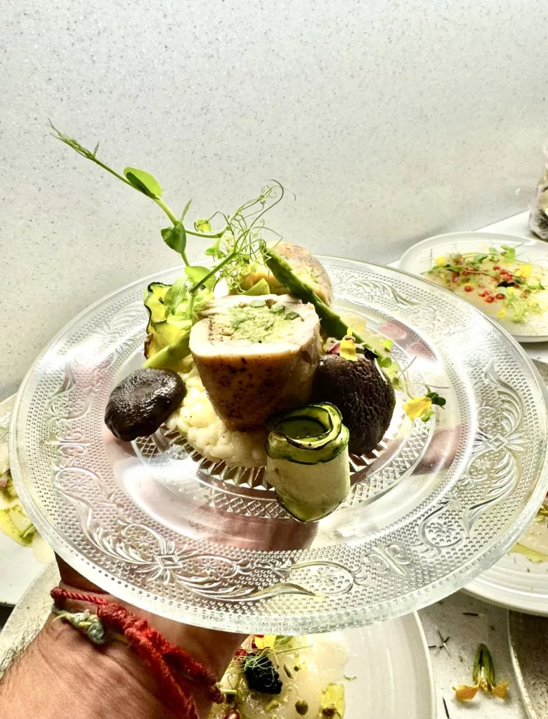 Plated main course with a roulade, green vegetables and herbs on a vintage glass plate at a Marbella wedding