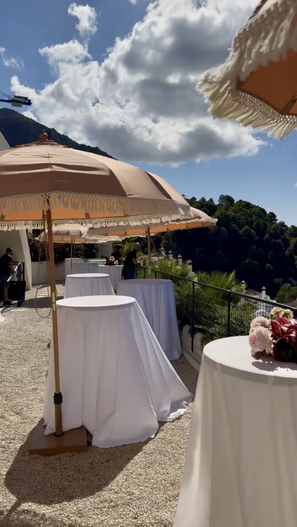 Fringed beige parasol and cocktail tables with white cloths on a terrace with a mountain view in Marbella