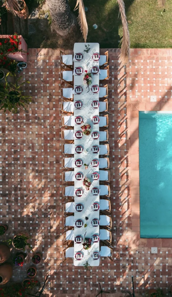 Aerial view of a long banquet table on a terracotta terrace next to a swimming pool, wedding in Marbella