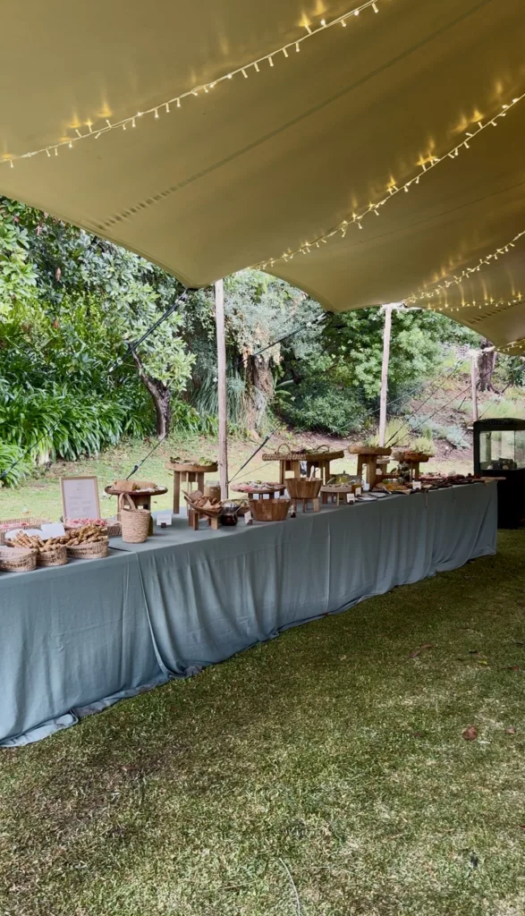Wedding buffet table with blue linen under a draped tent with fairy lights in a Marbella garden